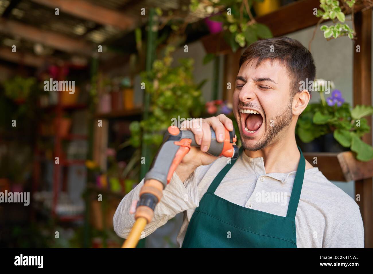 Giovane giardiniere con un tubo da giardino che canta forte da joie de vivre Foto Stock