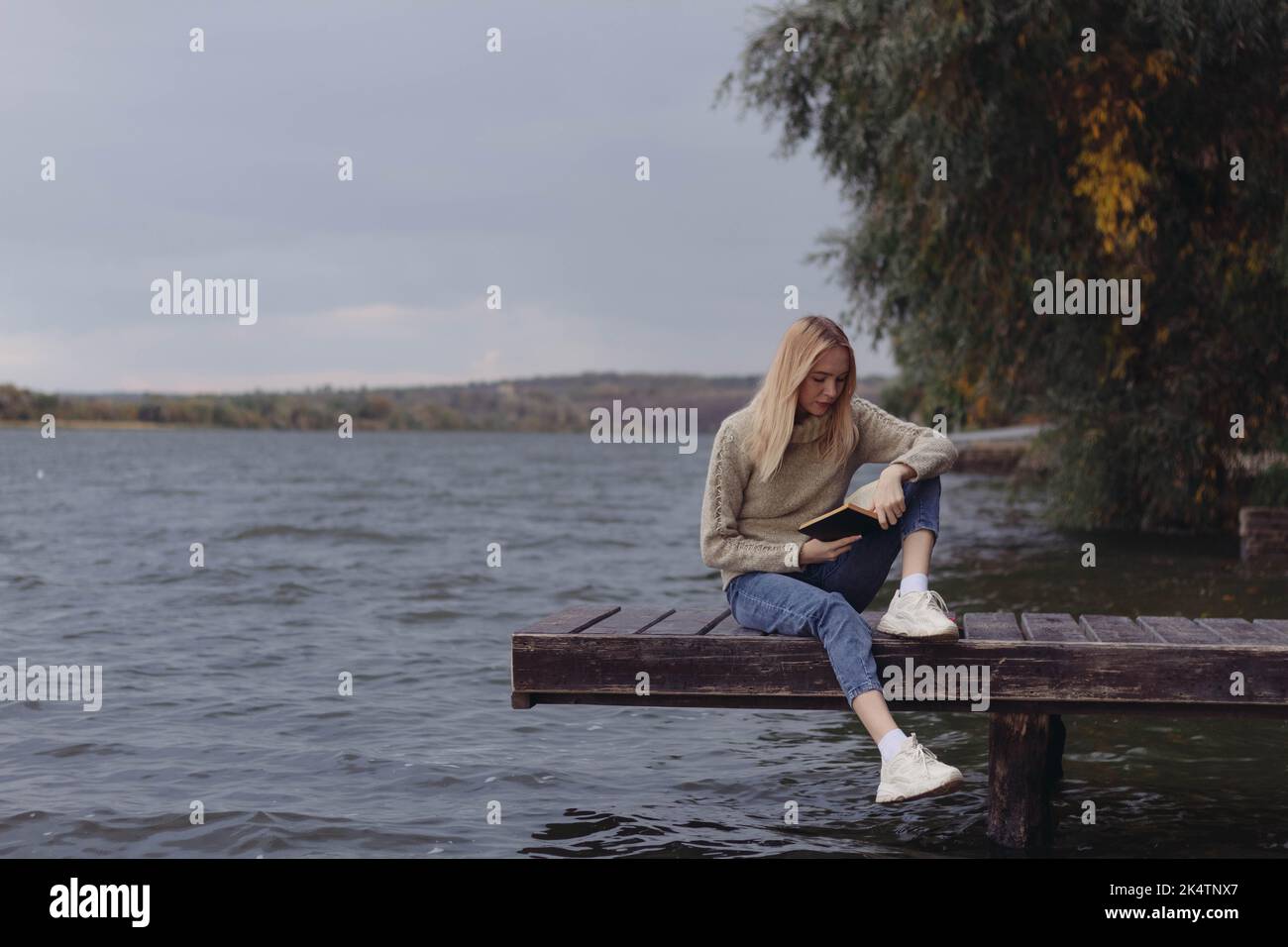 In autunno, una ragazza sulla riva del fiume legge un libro Foto Stock