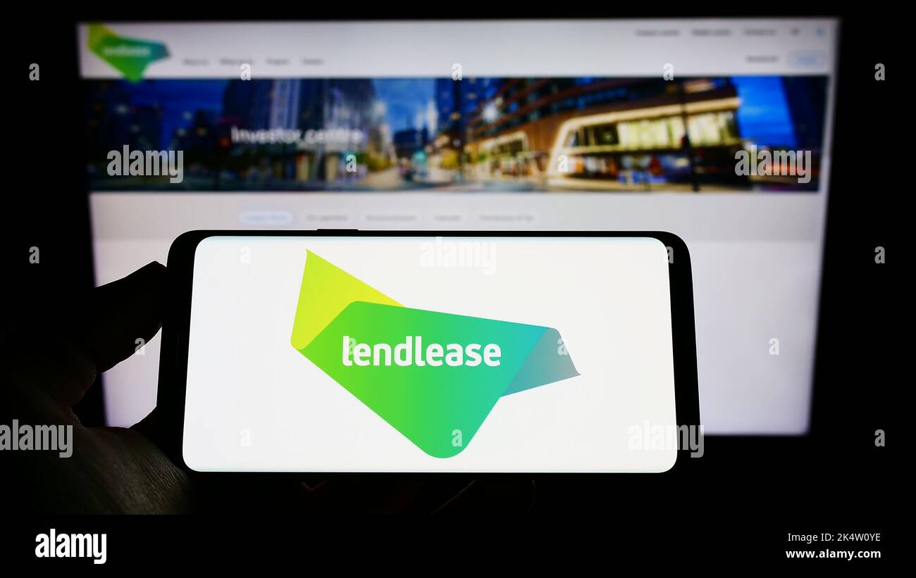 Persona che tiene il cellulare con il logo della società immobiliare Lendlease Corporation Limited sullo schermo di fronte al sito web. Messa a fuoco sul display del telefono. Foto Stock