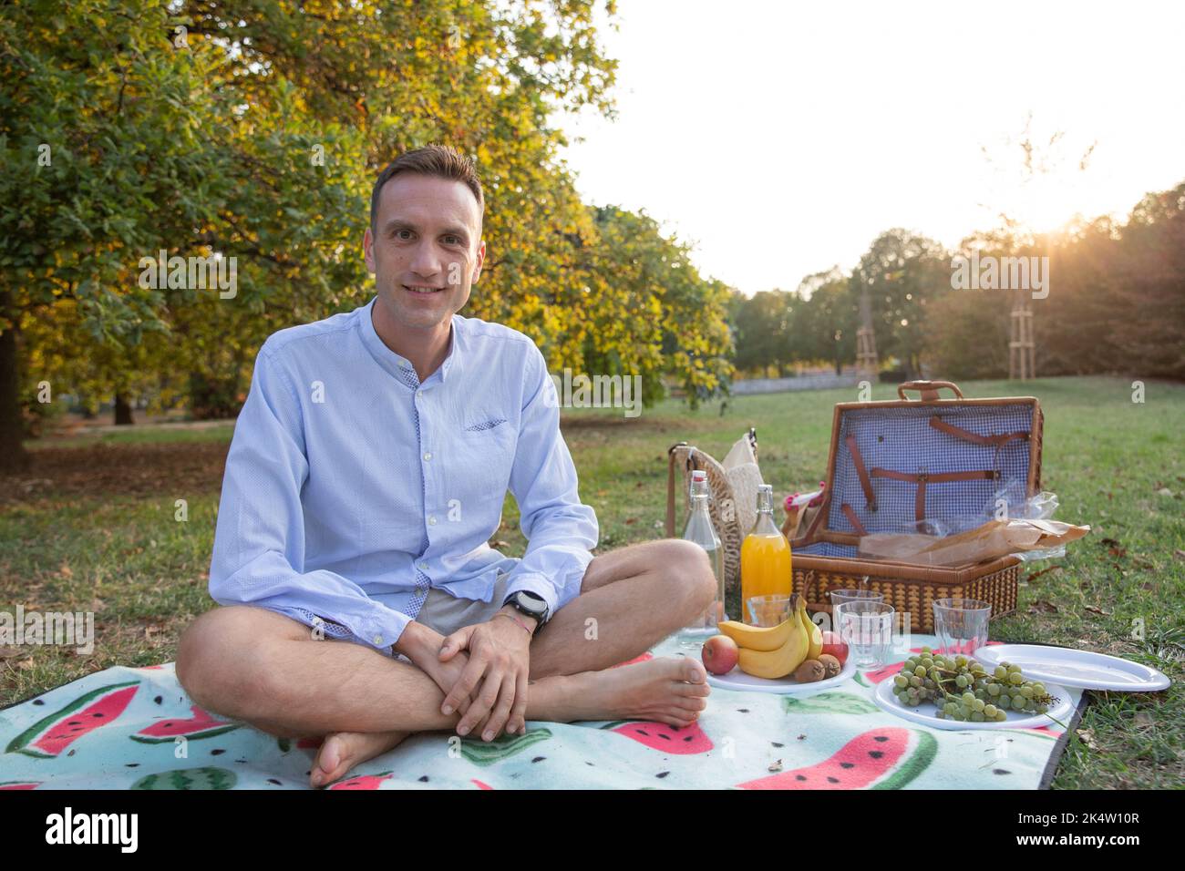 L'uomo nel suo 30s, con cibi vegani accanto a lui sorride seduto su coperta da picnic, copia spazio sulla destra. Foto Stock