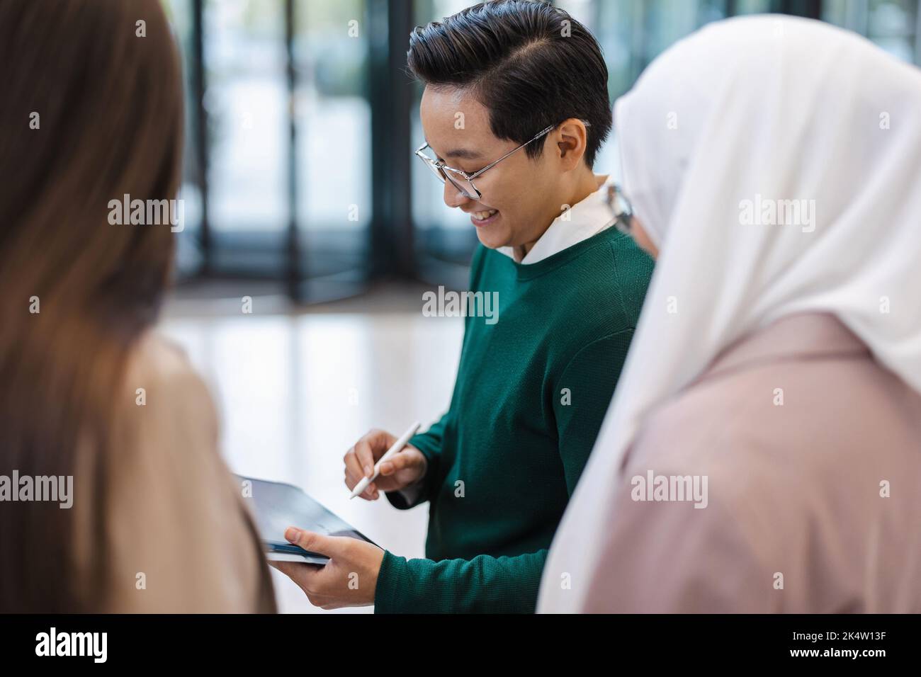 Giovane uomo d'affari che mostra qualcosa ai suoi colleghi sul tablet in ufficio Foto Stock