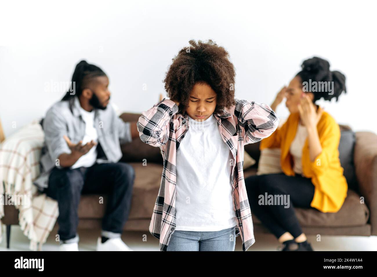 Infelice triste bambina afroamericana, chiuso gli occhi e le orecchie, sentirsi solo senza l'attenzione dei genitori, soffrono di conflitti familiari domestici, genitori sullo sfondo urla l'un l'altro Foto Stock