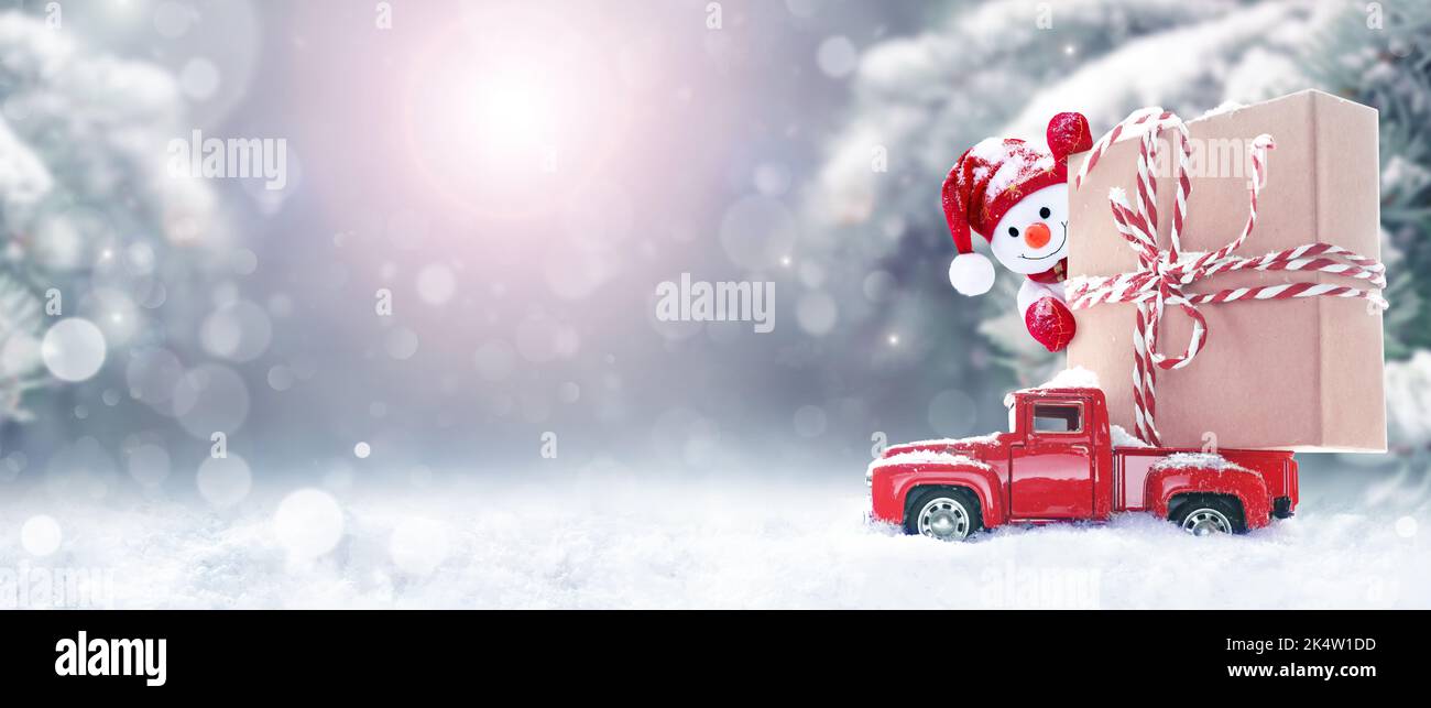 Sfondo natalizio con neve, pupazzo di neve e auto rossa retrò con scatola regalo. Buon Natale e Felice Capodanno con copyspace Foto Stock