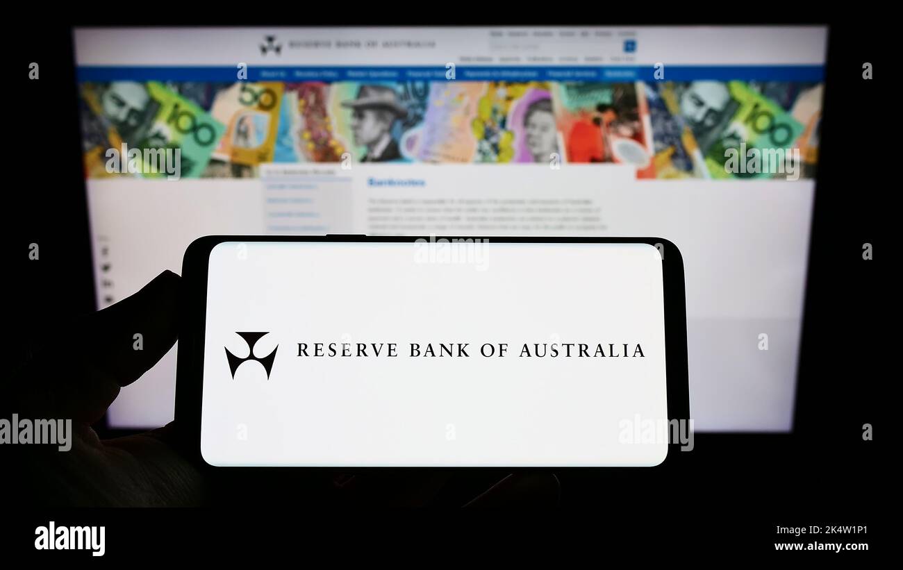 Persona in possesso di smartphone con il logo dell'emittente Reserve Bank of Australia (RBA) sullo schermo di fronte al sito Web. Messa a fuoco sul display del telefono. Foto Stock