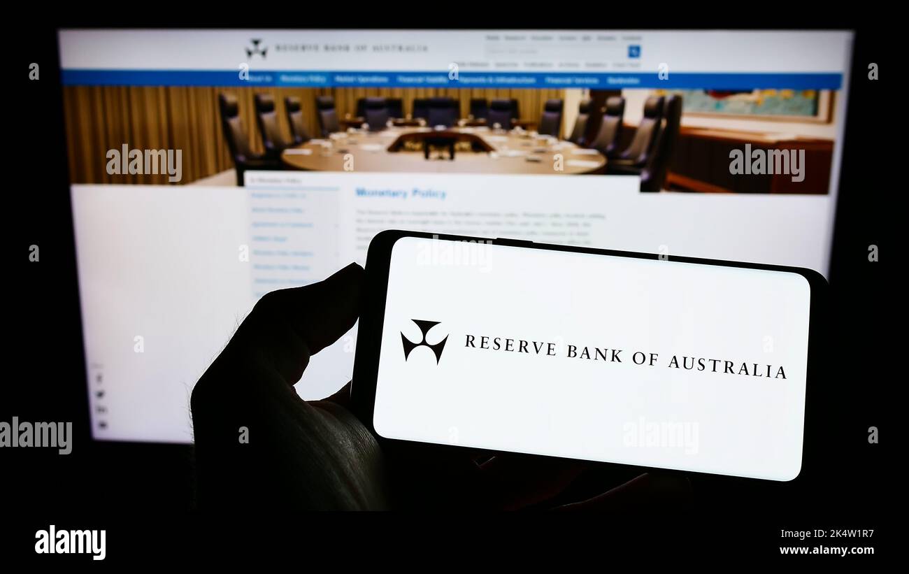 Persona che tiene il cellulare con il logo dell'emittente Reserve Bank of Australia (RBA) sullo schermo di fronte alla pagina web aziendale. Messa a fuoco sul display del telefono. Foto Stock