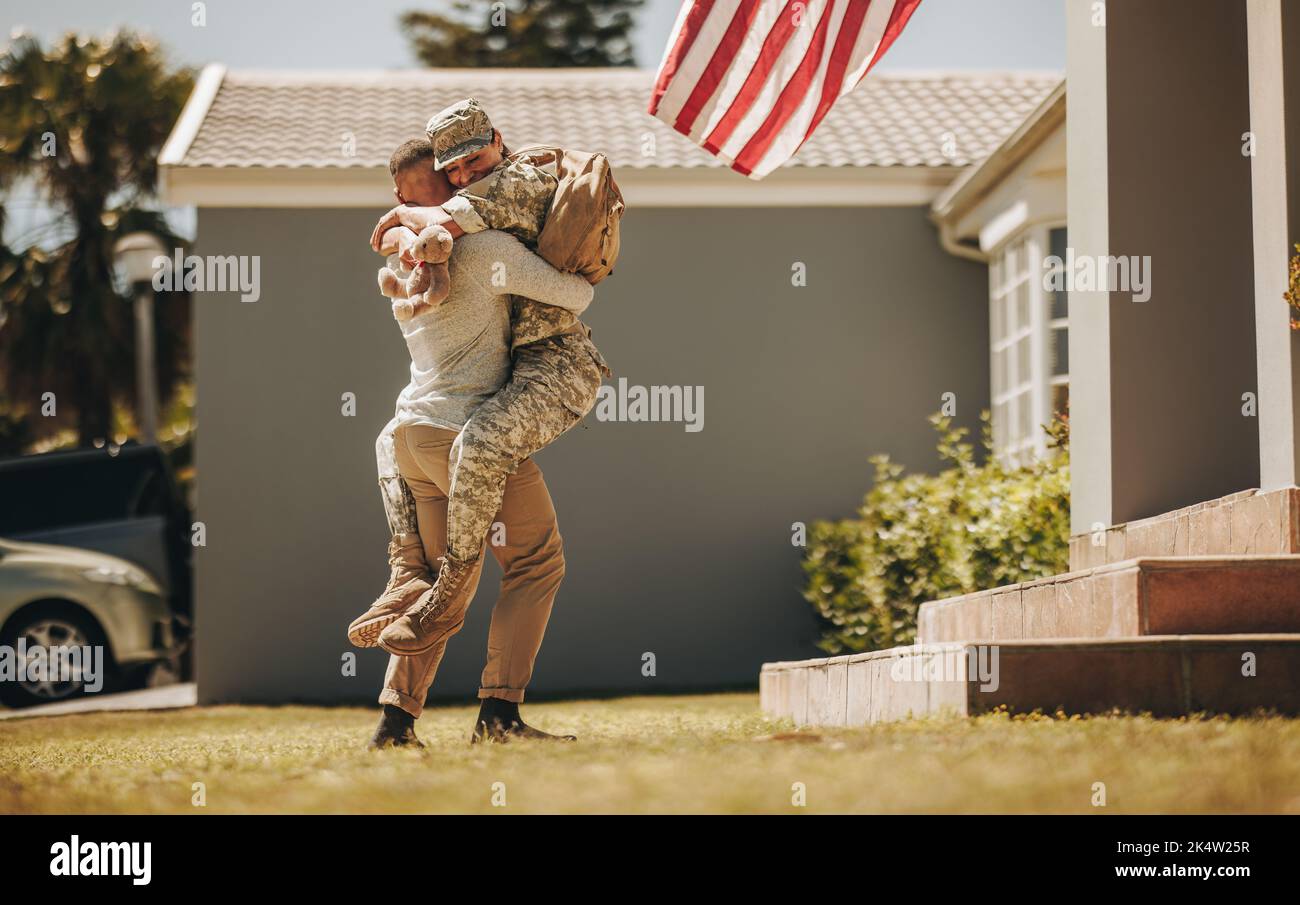Gioiosa casa militare. Un soldato allegro che abbraccia il marito dopo essere tornato a casa dall'esercito. Americano servicewoman riunendosi con il suo marito Foto Stock
