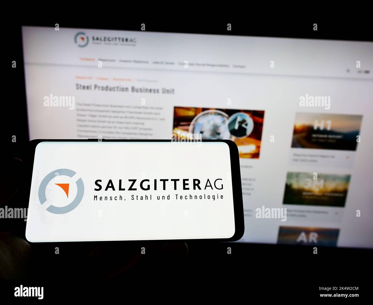 Persona che tiene il cellulare con il logo della società siderurgica tedesca Salzgitter AG sullo schermo di fronte alla pagina web aziendale. Messa a fuoco sul display del telefono. Foto Stock