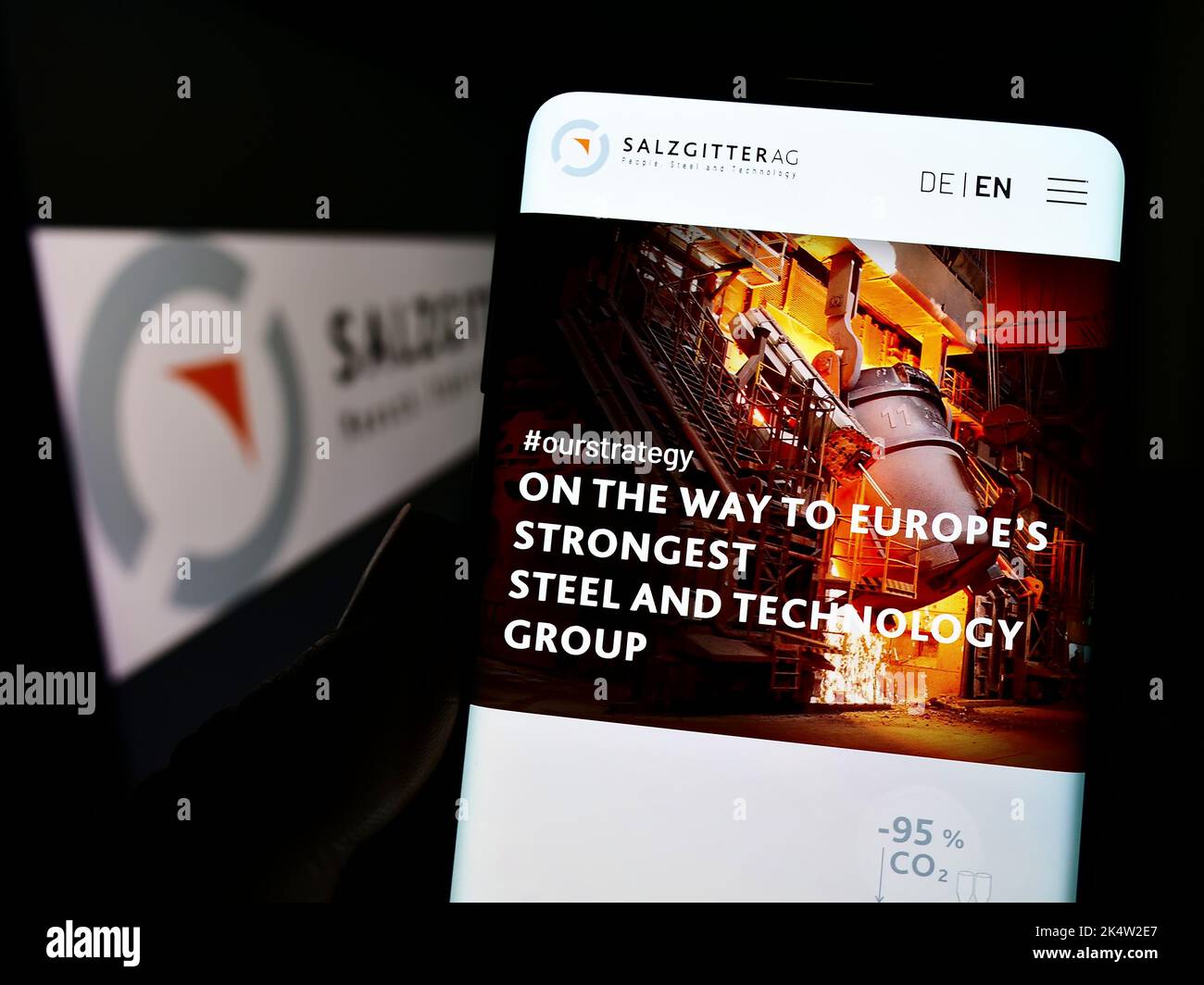 Persona che tiene il cellulare con la pagina web della società siderurgica tedesca Salzgitter AG sullo schermo di fronte al logo. Messa a fuoco al centro del display del telefono. Foto Stock