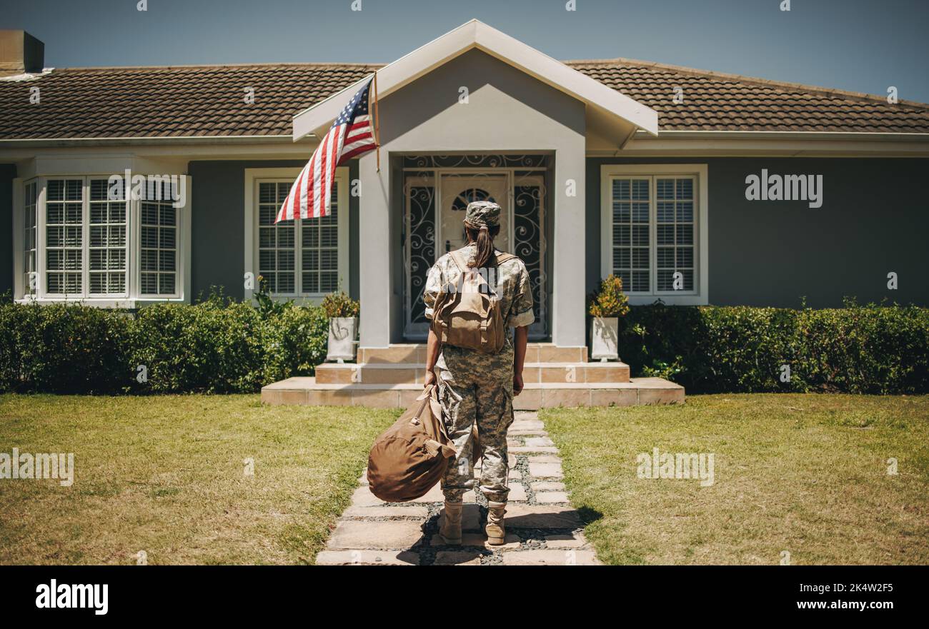 Vista posteriore di una soldato patriottica in piedi di fronte alla sua casa con i suoi bagagli. Coraggioso servicewoman tornare a casa dopo aver servito il suo paese Foto Stock