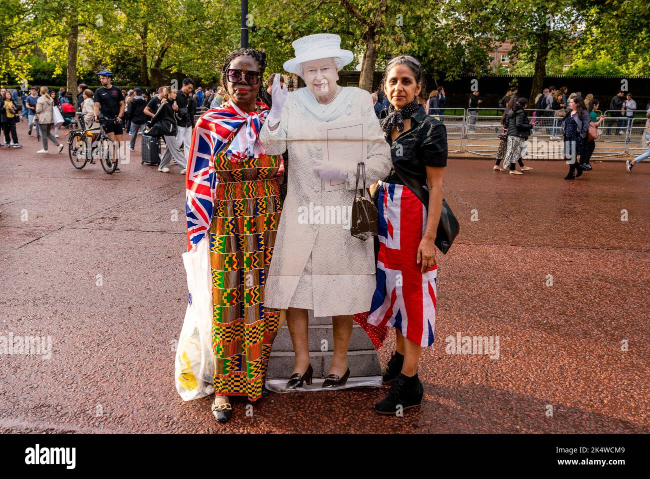 Il giorno dopo la morte della Regina Elisabetta II due donne portano Con sé Un taglio di cartone a grandezza naturale della Regina in Tribute, The Mall, Londra, Regno Unito. Foto Stock