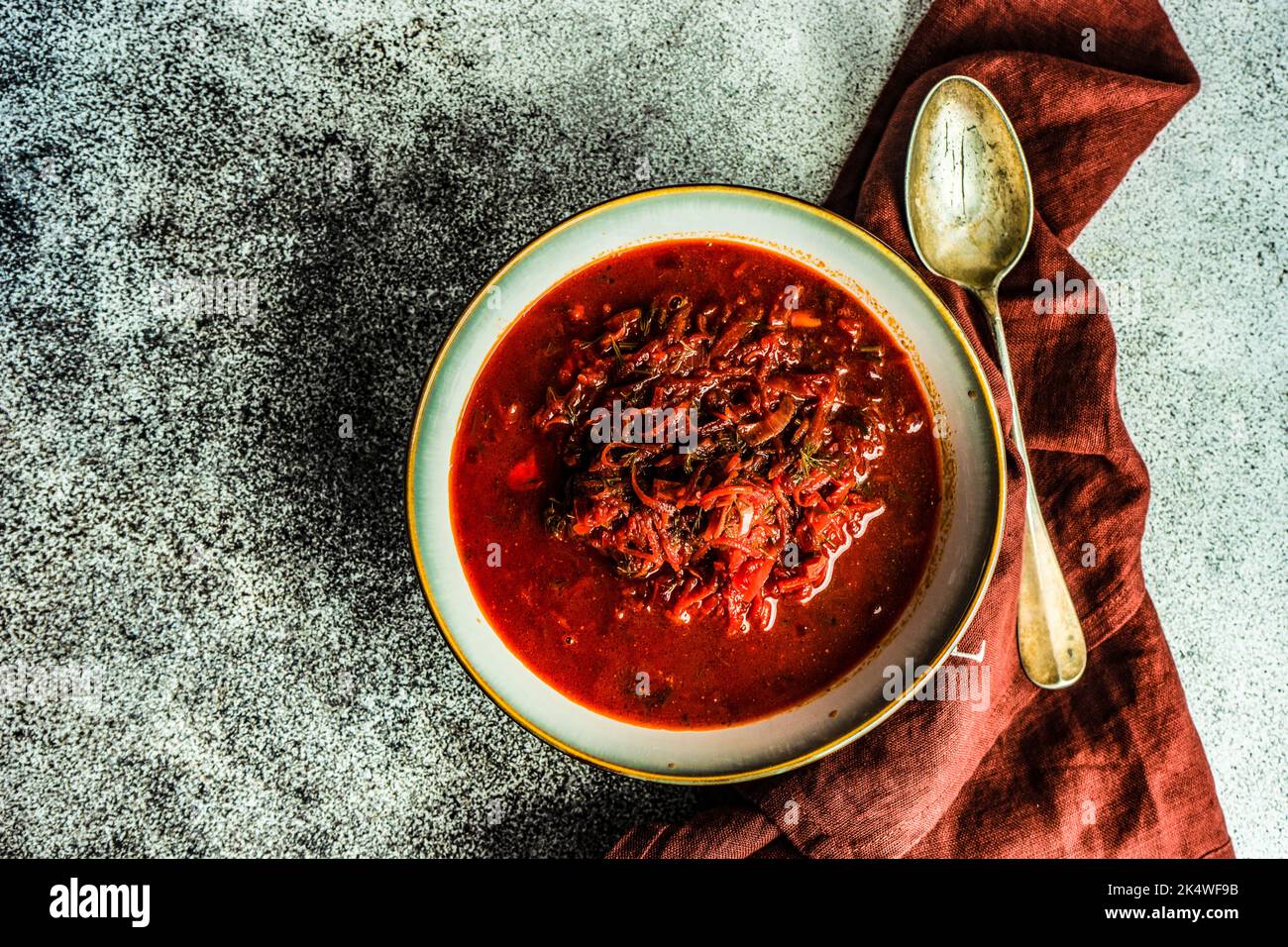 Vista dall'alto di una ciotola di zuppa tradizionale Ucraina di barbabietole (borscht) su un tavolo con un cucchiaio e tovagliolo Foto Stock