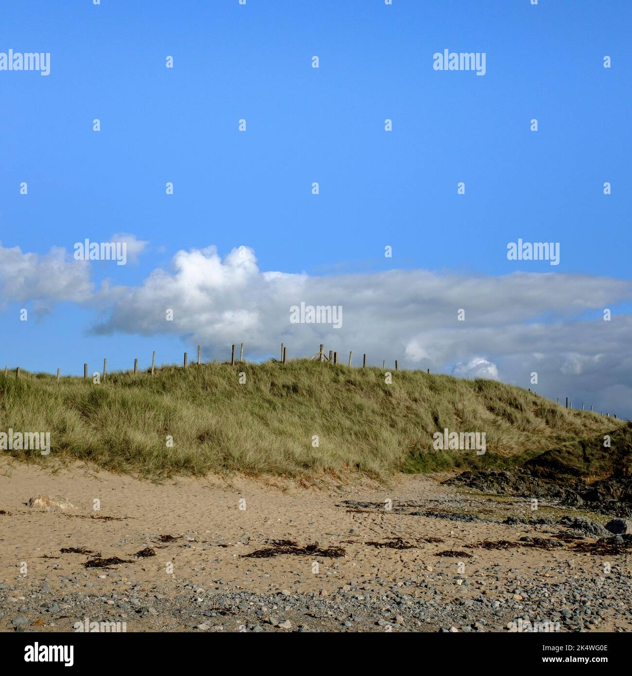 Nuvole bianche in un cielo blu chiaro sopra le dune di sabbia a Rhosneigr, Galles del Nord, Regno Unito Foto Stock