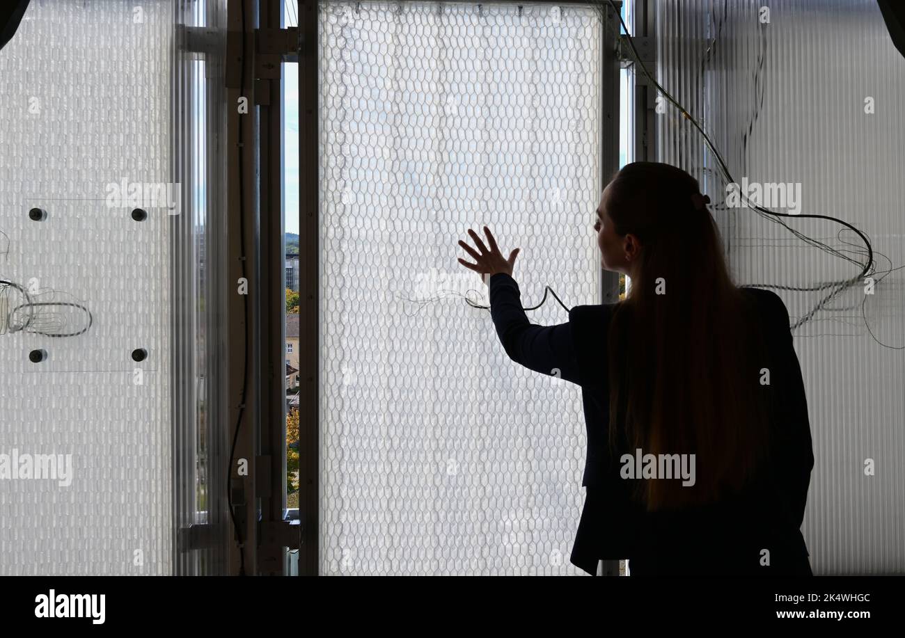 Stoccarda, Germania. 04th Ott 2022. Christina Eisenbarth dell'Istituto di Design e costruzione leggera (ILEK) dell'Università di Stoccarda si trova di fronte agli elementi tessili della facciata in un edificio di ricerca in grado di assorbire l'acqua piovana e di utilizzarla per il raffreddamento quando è calda. Gli elementi tessili della facciata attaccati all'alto-edificio assorbono l'acqua quando piove e lo rilasciano di nuovo nelle giornate calde per raffreddamento evaporativo. Ciò è inteso a ridurre i rischi di allagamento e calore con un uso minimo dei materiali. Credit: Bernd Weißbrod/dpa/Alamy Live News Foto Stock