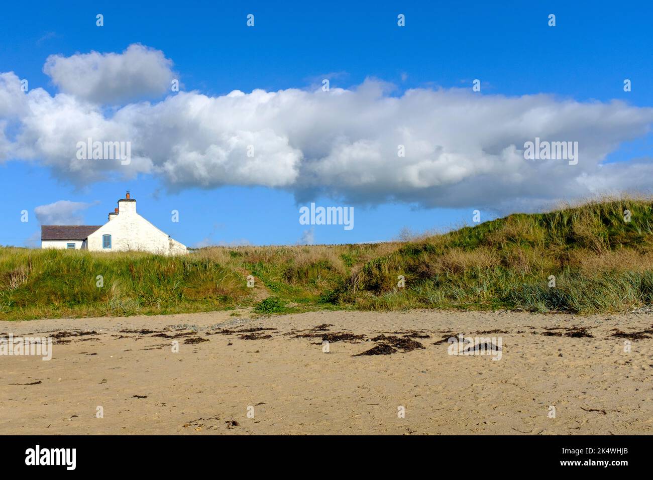 Nuvole bianche in un cielo blu chiaro sopra un cottage semplice sopra le dune di sabbia a Rhosneigr, Galles del Nord, Regno Unito Foto Stock