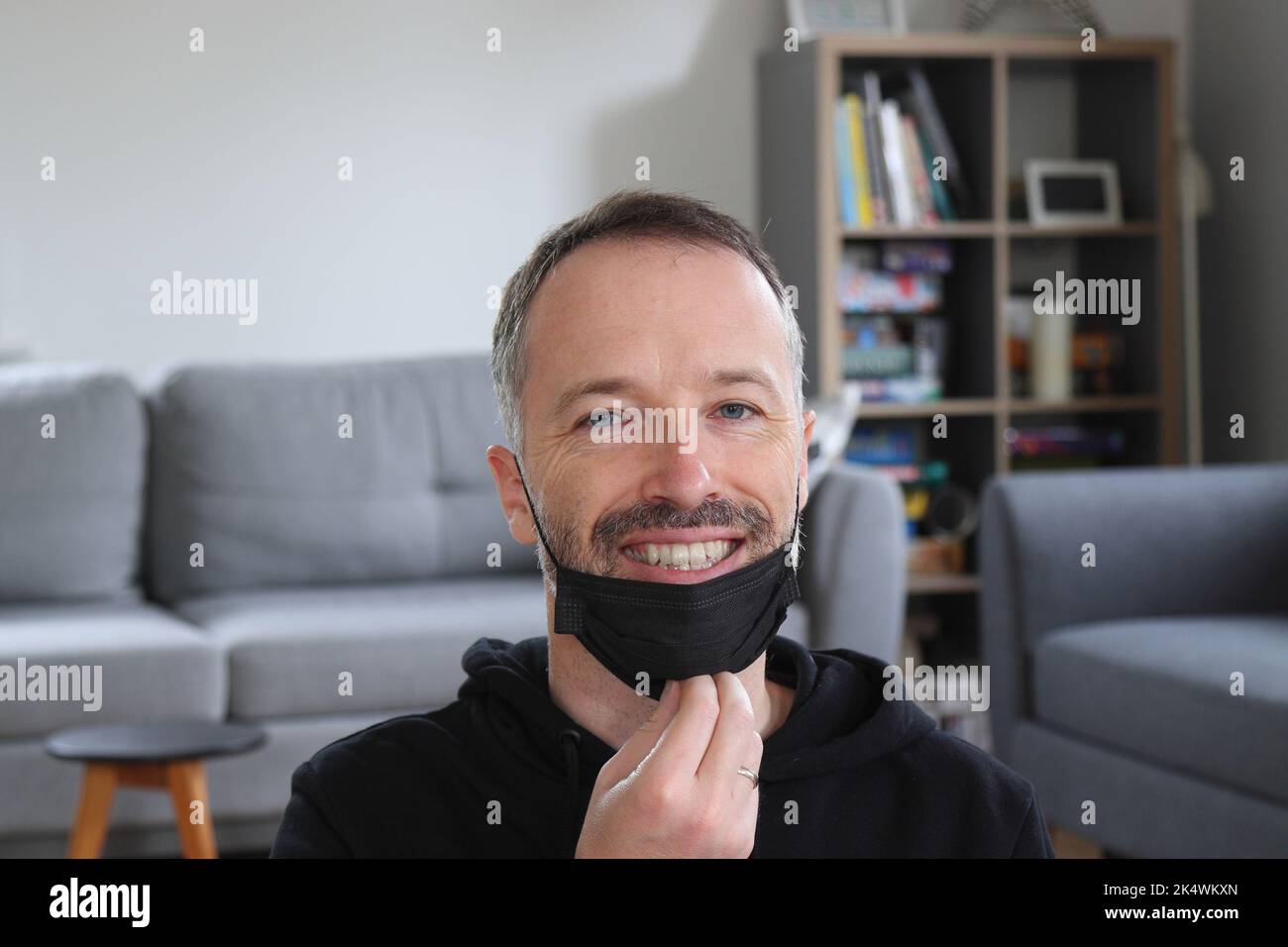 Persona che tira giù la maschera facciale. Uomo bearded con cappuccio nero casual. Uomo caucasico adulto di 30s o 40s anni. Foto Stock