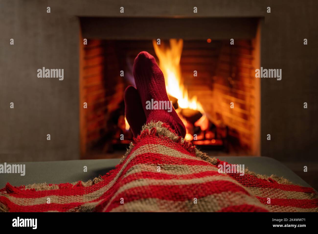 L'uomo che copre con coperta gode della calma accanto al camino che brucia. Inverno vacanze camino e fiamme sfondo, caldo casa interna. Foto Stock