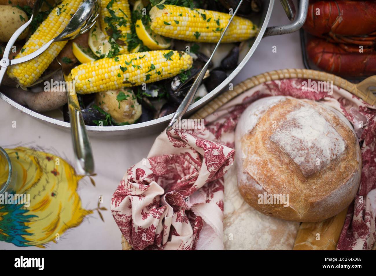 Foto di un clambake su un tavolo con aragosta, pane e mais Foto Stock