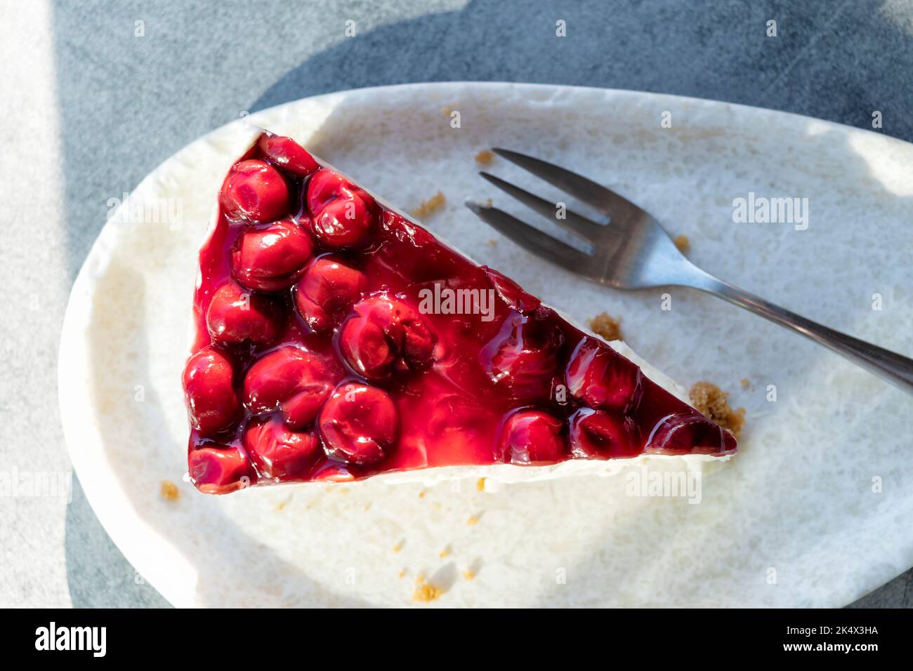 Una vista dall'alto di una singola fetta, o servizio, di fresco, indulgente torta di formaggio di ciliegia. E' servito su un piatto su un tavolo esterno in un cafe'. Foto Stock