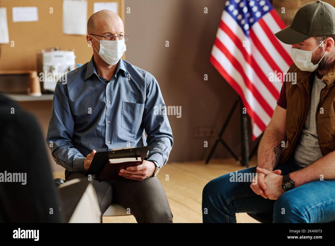 Psicoterapeuta maschile matura in maschera protettiva ascoltando pazienti con sindrome post traumatica a sessione psicologica Foto Stock