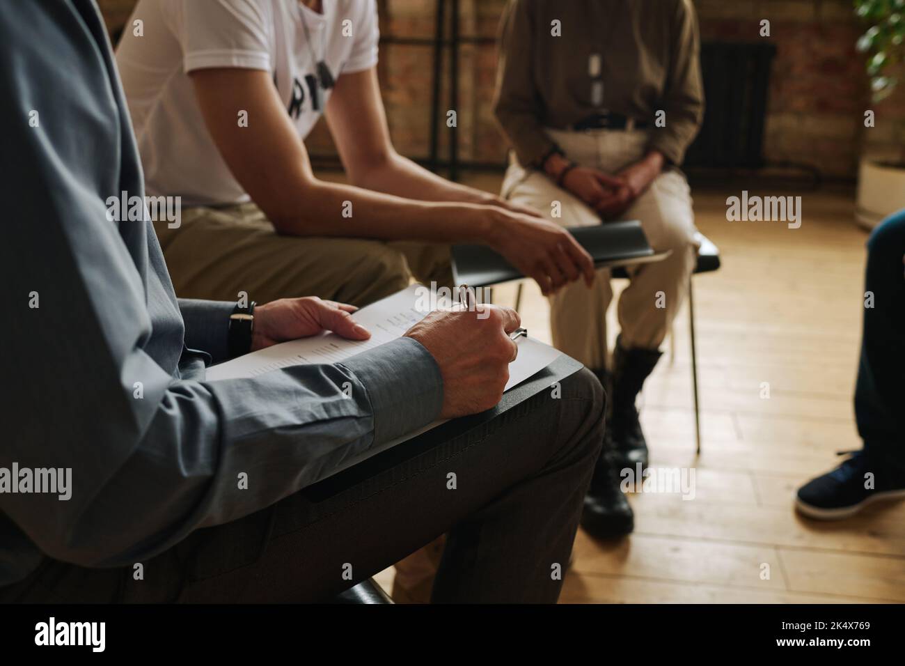 Primo piano del consulente professionale compilando il modulo mentre si annotano le informazioni sui suoi pazienti con PTSD durante la sessione psicologica Foto Stock
