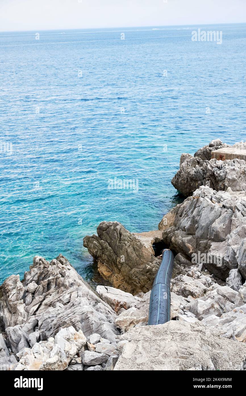 Lungo tubo nero inquinare il mare e l'acqua con rifiuti tossici. Concetto di conservazione ambientale Foto Stock