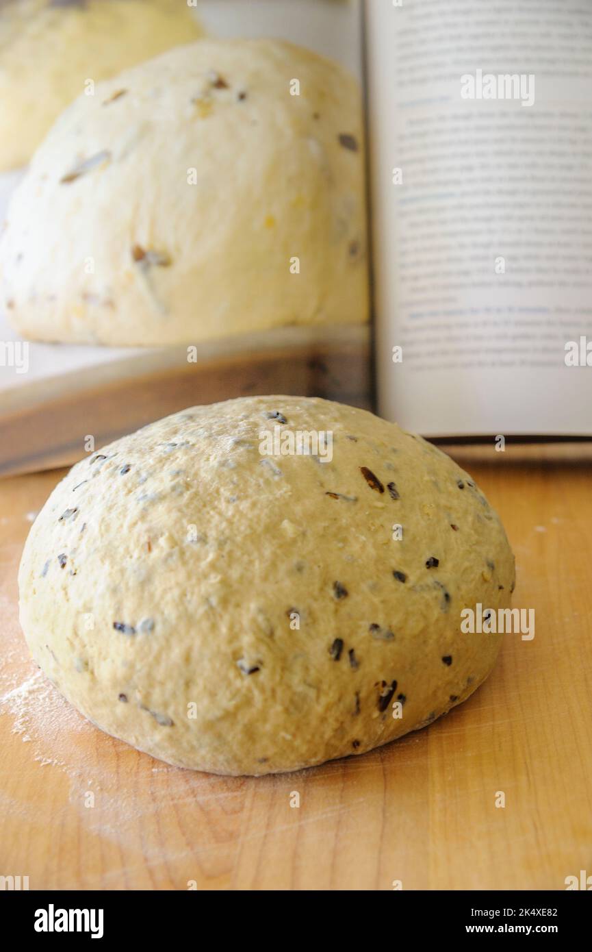 una palla di pasta di pane artissinale su un pannello di legno con un libro di ricette sfocato sullo sfondo Foto Stock