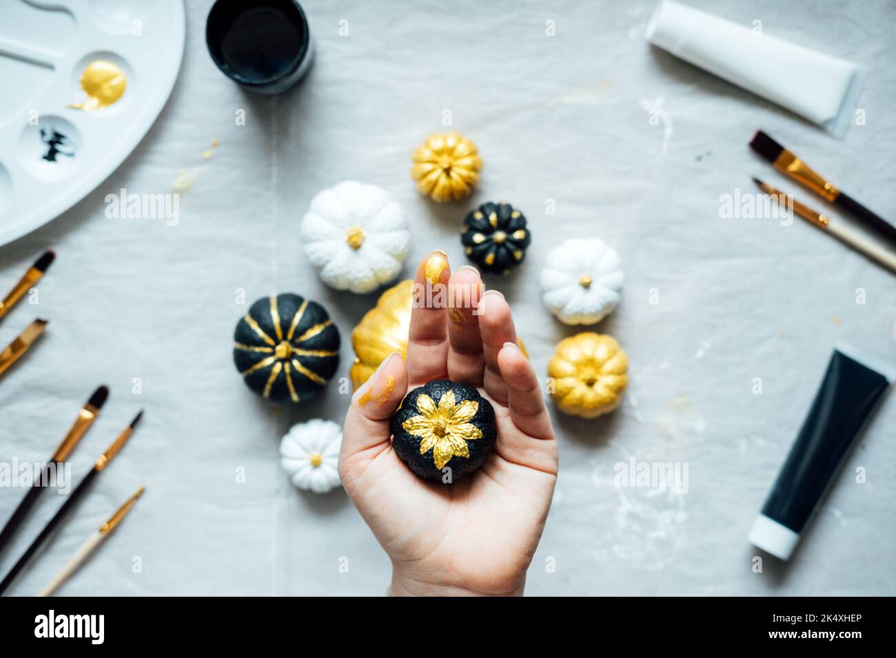 Sfondo di idee artigianali di Halloween con zucca di Halloween nera e d'oro. Le mani femminili con la zucca di pittura creativa per Halloween e il giorno del Ringraziamento Foto Stock