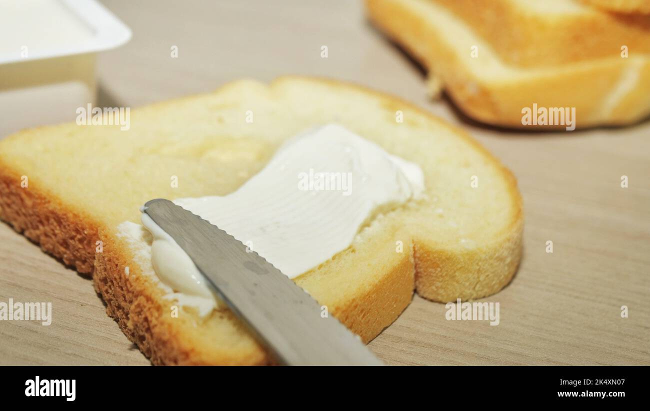 Stendere il burro sul toast con il coltello sul pannello di legno Foto Stock