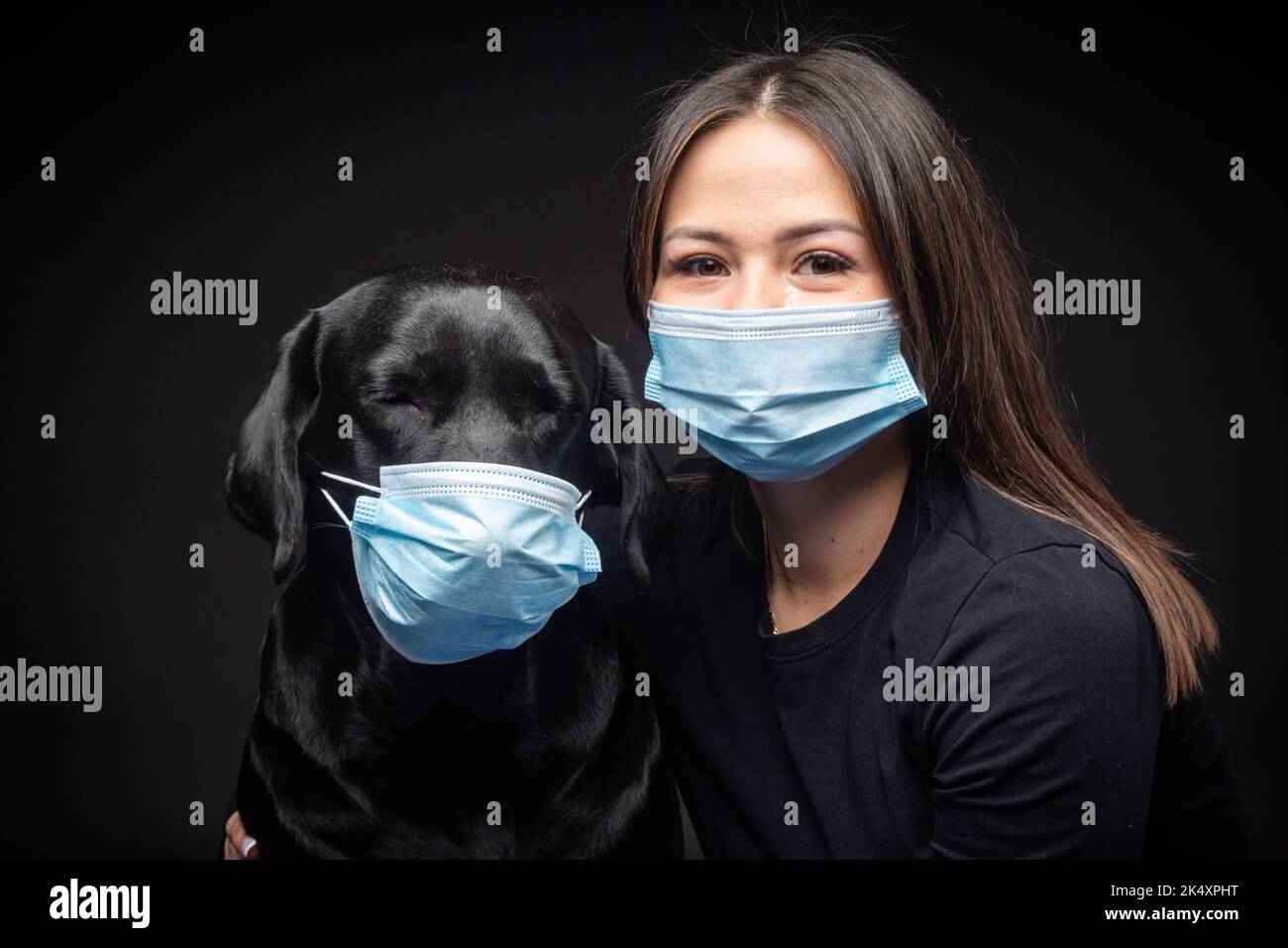 Ritratto di un cane Labrador Retriever in una maschera medica protettiva con una donna proprietario. La foto è stata scattata in uno studio fotografico Foto Stock