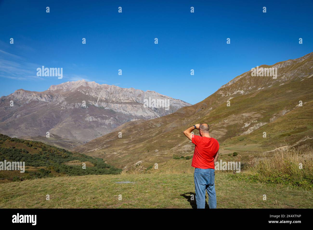 Un uomo si erge sulla cima di una montagna con le braccia tese Foto Stock