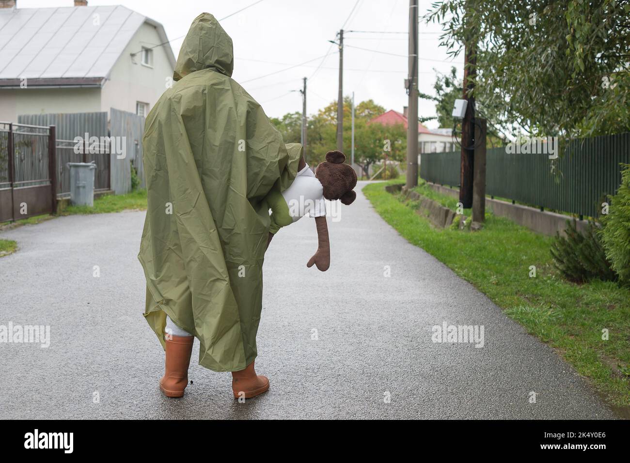 Ragazzo che indossa un impermeabile verde in piedi sulla strada durante le giornate di pioggia. Ritratto dei bambini in autunno tempo freddo. Tenendo il giocattolo morbido della scimmia. Copia spazio per il testo. Foto Stock