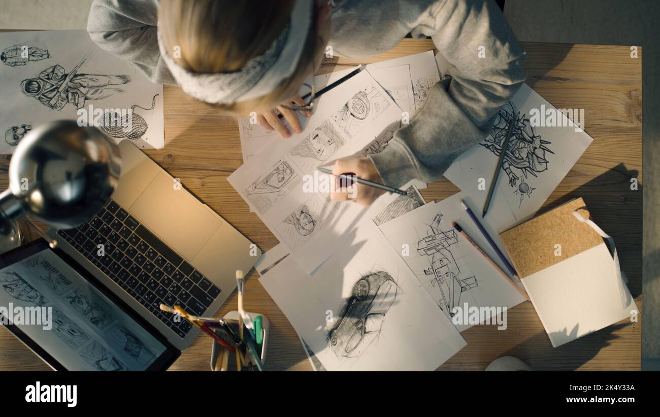 Giovane donna che lavora a uno storyboard in uno studio di design. Un computer portatile e un vasetto fisso sul tavolo. Donna che disegna gli schizzi come roadmap per il video. Foto Stock