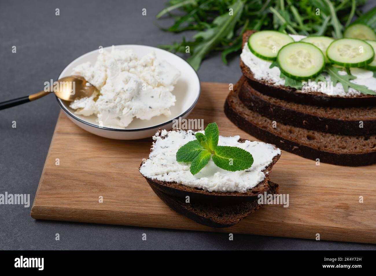 Fette di pane di segale con formaggio casereccio e cetrioli su sfondo grigio Foto Stock