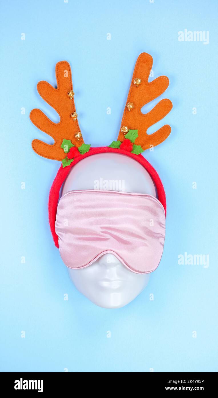 Maschera a occhio dormiente rosa sul viso manichino con corna natalizie su sfondo blu, disturbi del sonno. Giorni festivi, accessorio testa. Superficie in plastica. Foto Stock