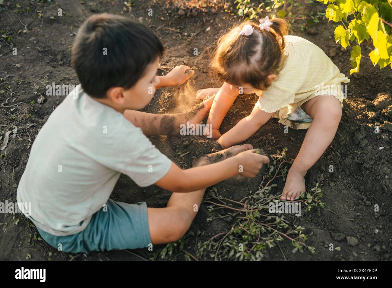 Felici due bambini che giocano all'aperto in giardino, con mani e gambe sporche. Splendido panorama. Divertimento per le vacanze estive. Piccolo giardino. Foto Stock