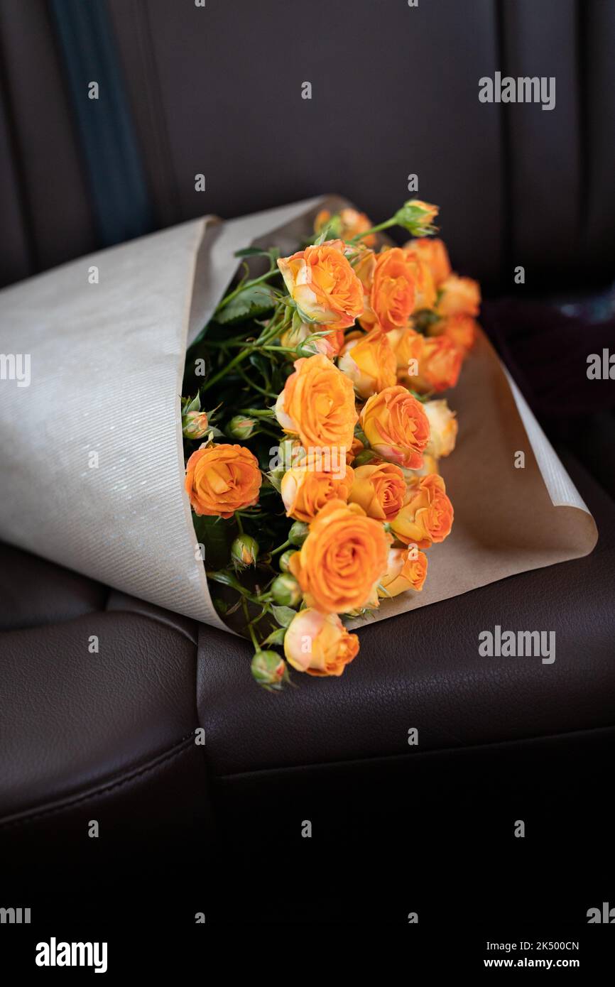 Un bouquet di rose arancioni sul sedile posteriore di un'auto con interni in pelle. Foto verticale. Foto Stock