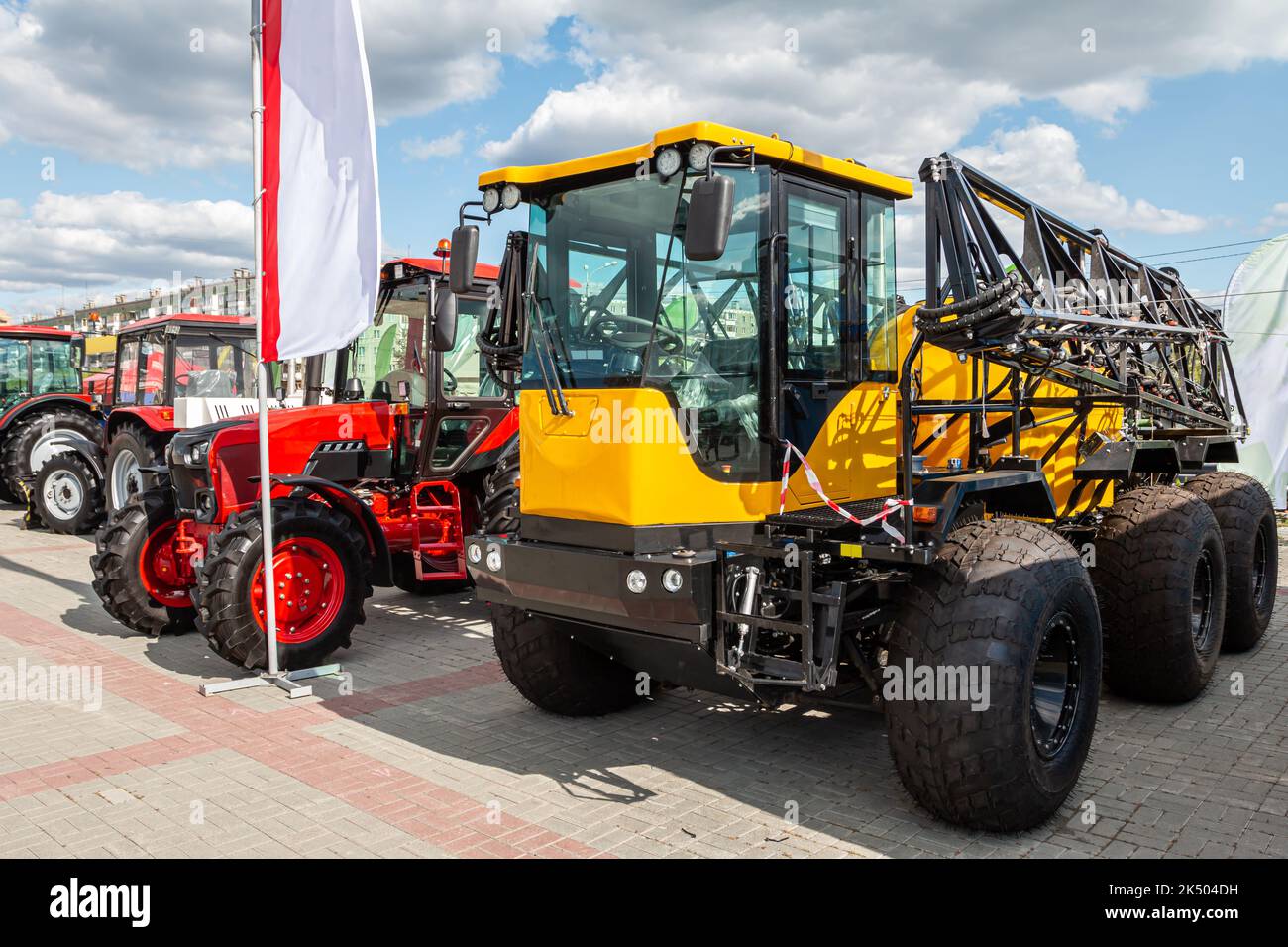 Veicolo agricolo giallo per tutti i terreni con attrezzatura di irrorazione sul campo e trattori gommati rossi Foto Stock