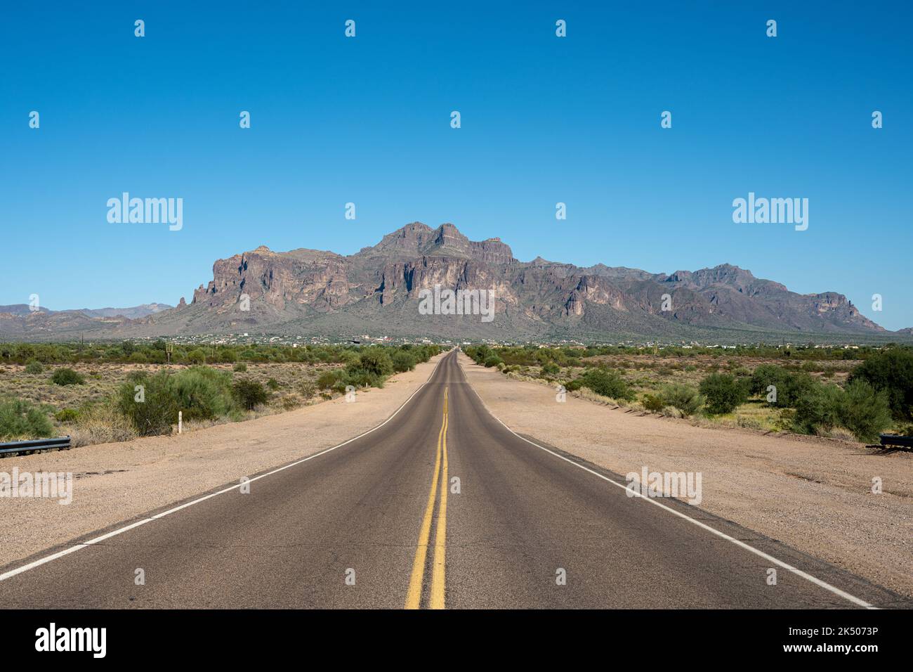 In piedi su una strada diritta che conduce alle Superstition Mountains Foto Stock