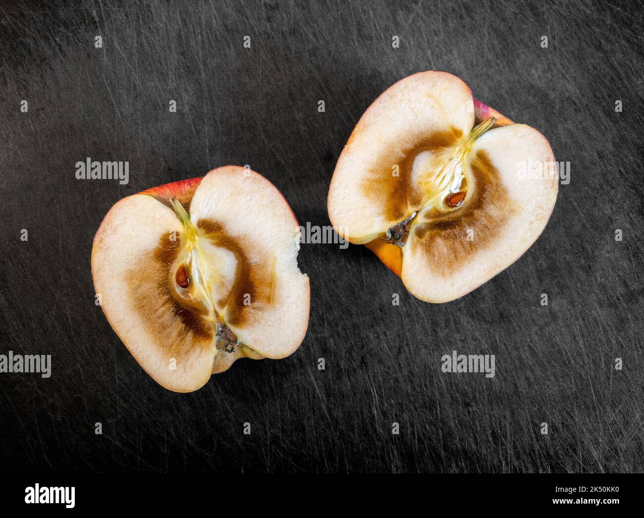 Due metà dell'interno di una mela tagliata aperta e marcietta, appoggiata sopra un tagliere scuro. Foto Stock