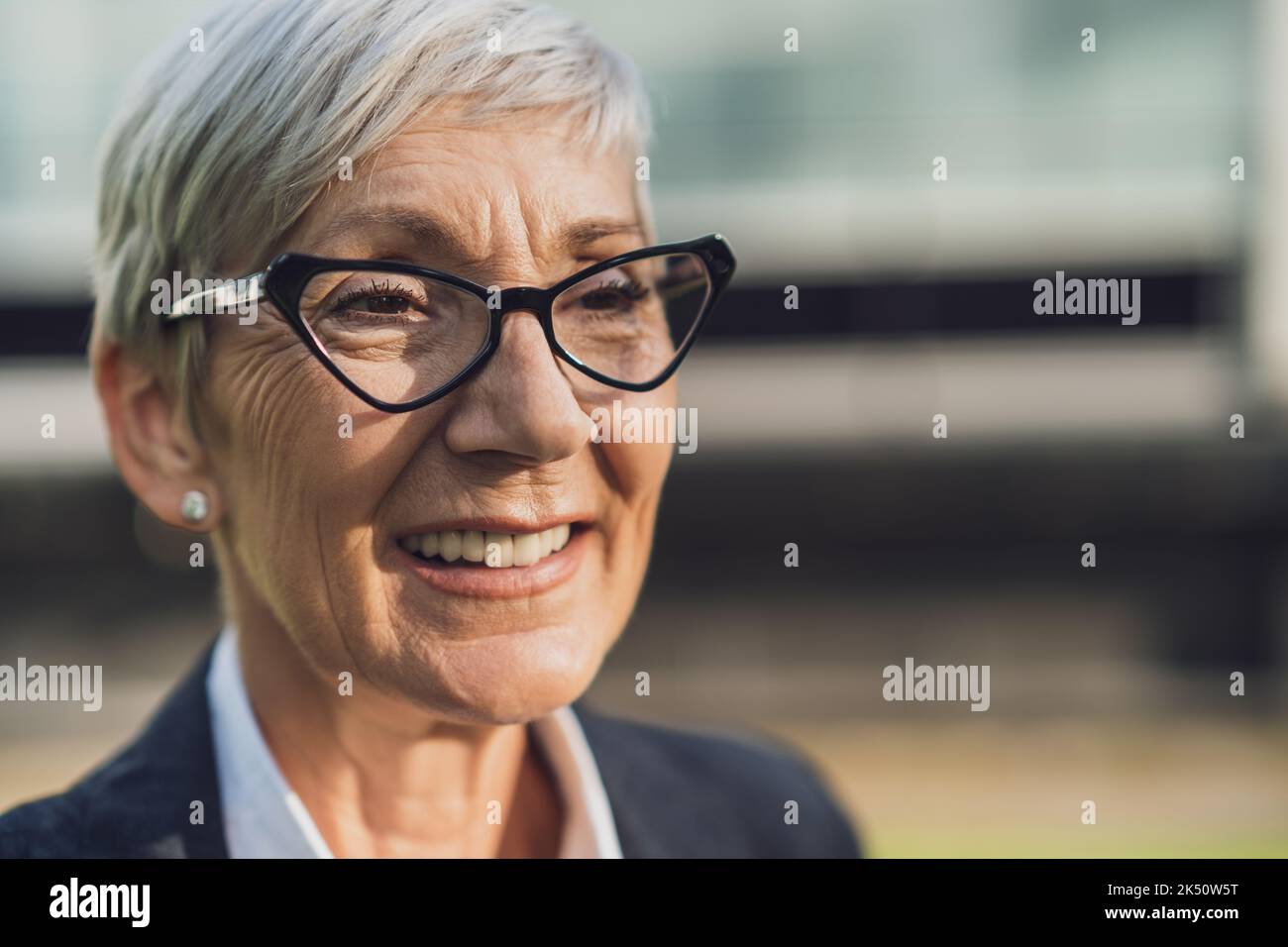 Ritratto della testa all'aperto di una donna d'affari anziana di successo. La persona felice di affari sta sorridendo e guardando via. Foto Stock