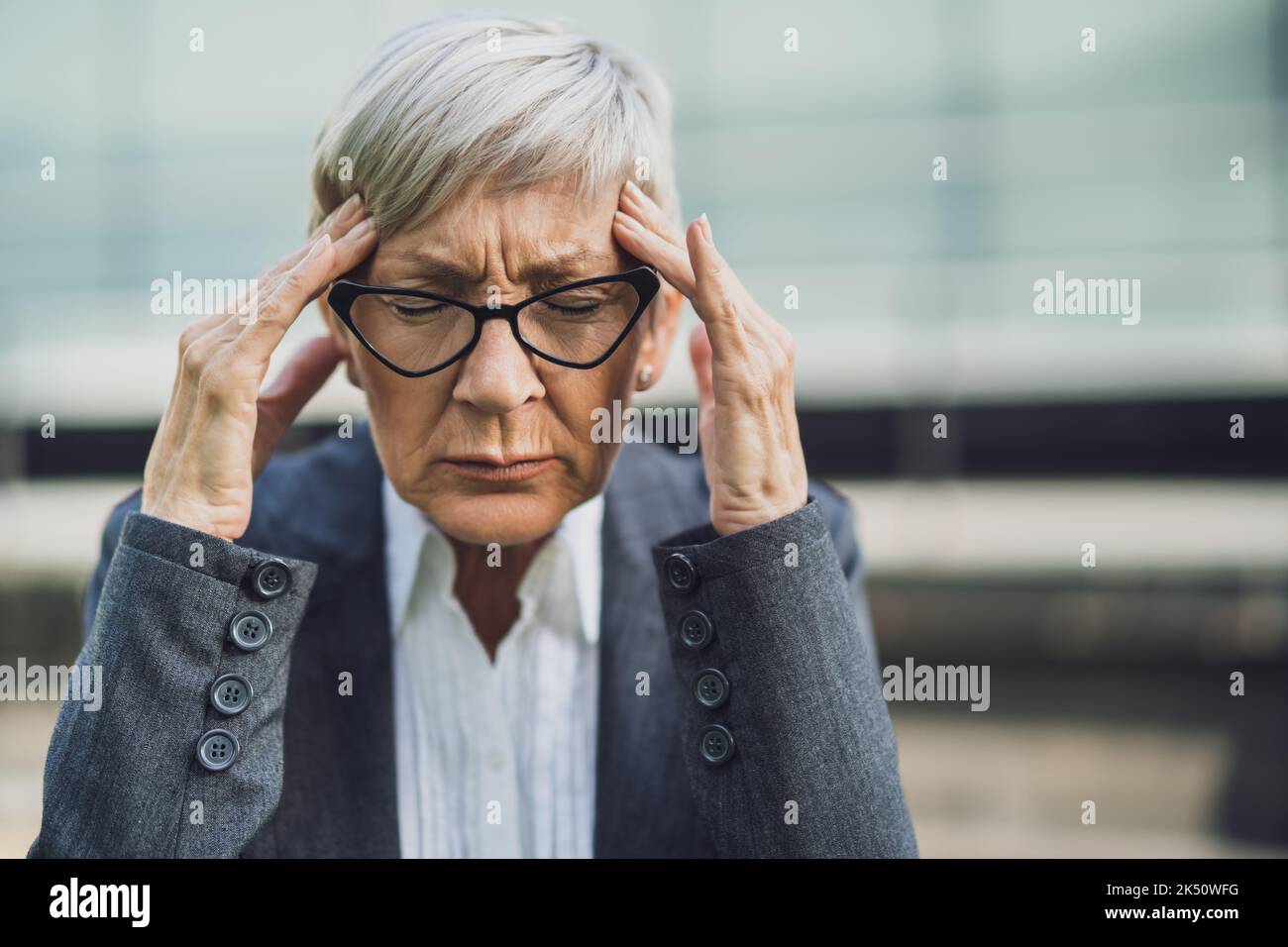 Primo piano ritratto di una donna d'affari anziana che è sovraccarica di lavoro e ha mal di testa. Foto Stock