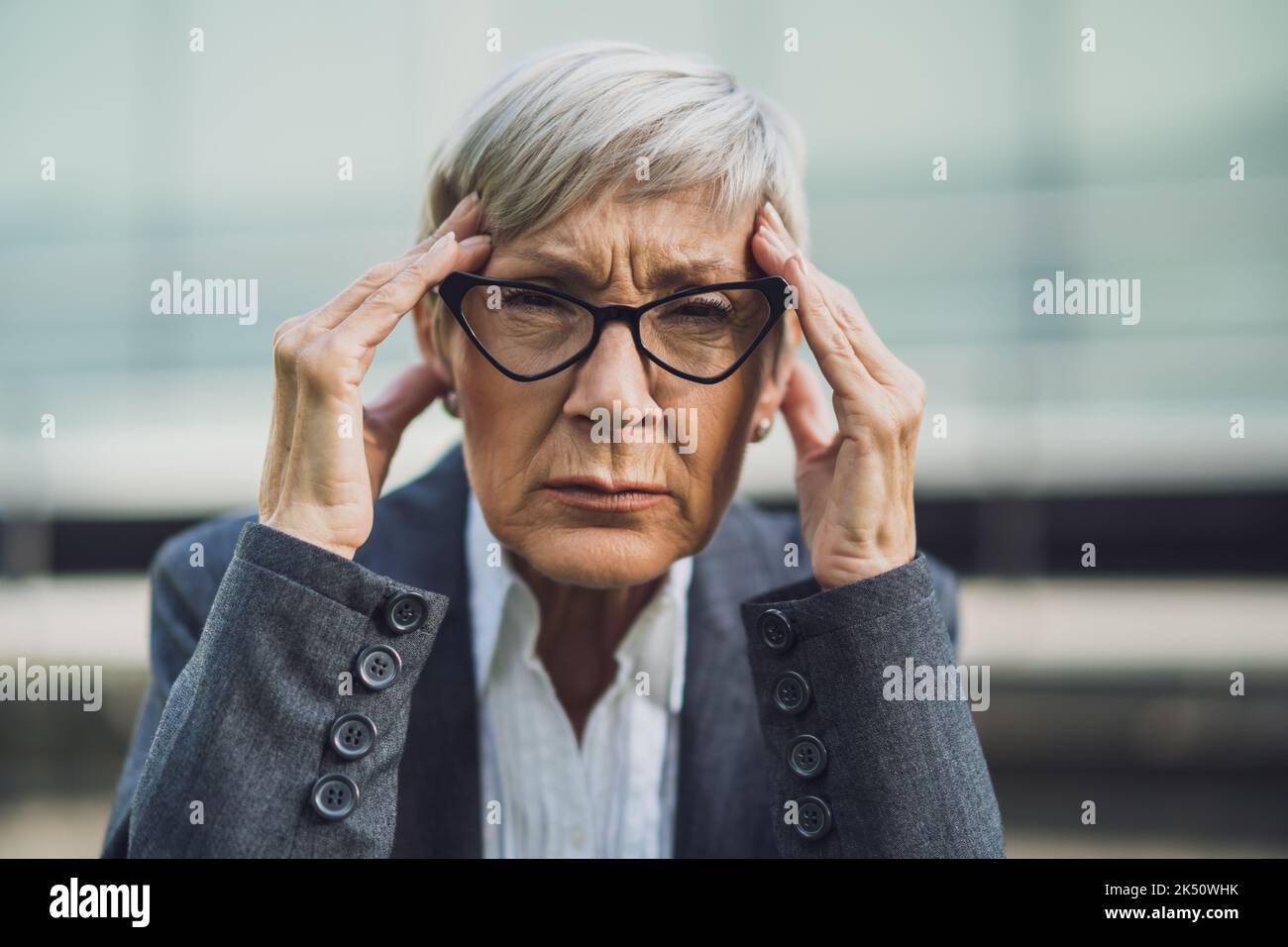 Primo piano ritratto di una donna d'affari anziana che è sovraccarica di lavoro e ha mal di testa. Foto Stock