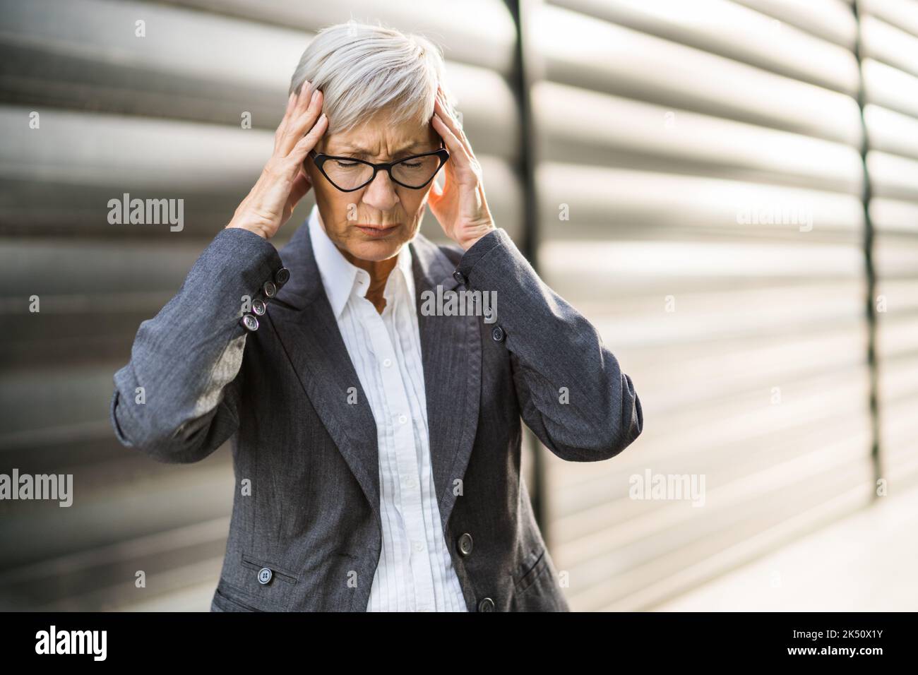Donna d'affari anziana sta avendo mal di testa. Si trova di fronte alla costruzione dell'azienda. Foto Stock