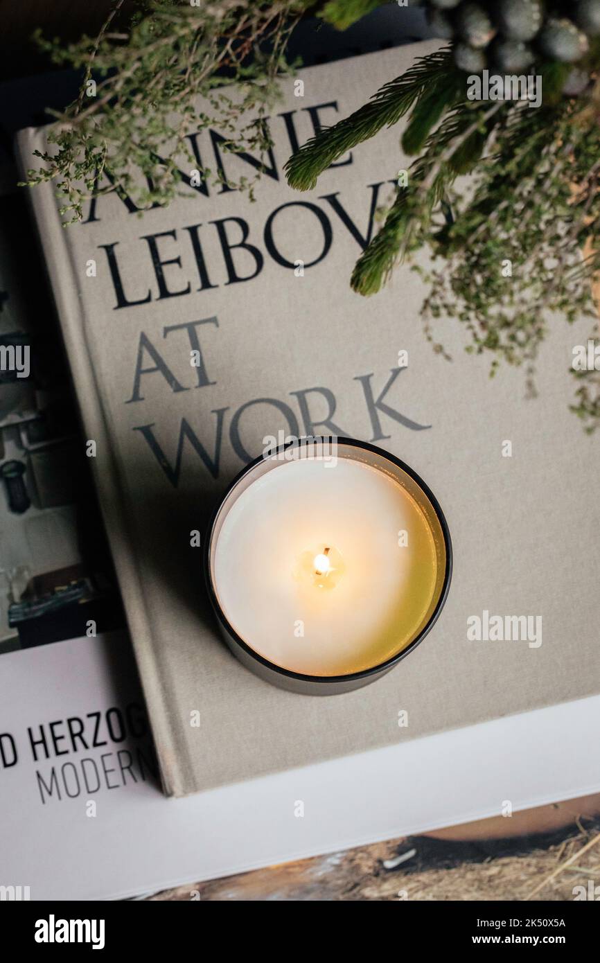 Soy Candle in un vaso di vetro verde seduto su una pila di libri in camera da letto tra fiori autunnali Foto Stock