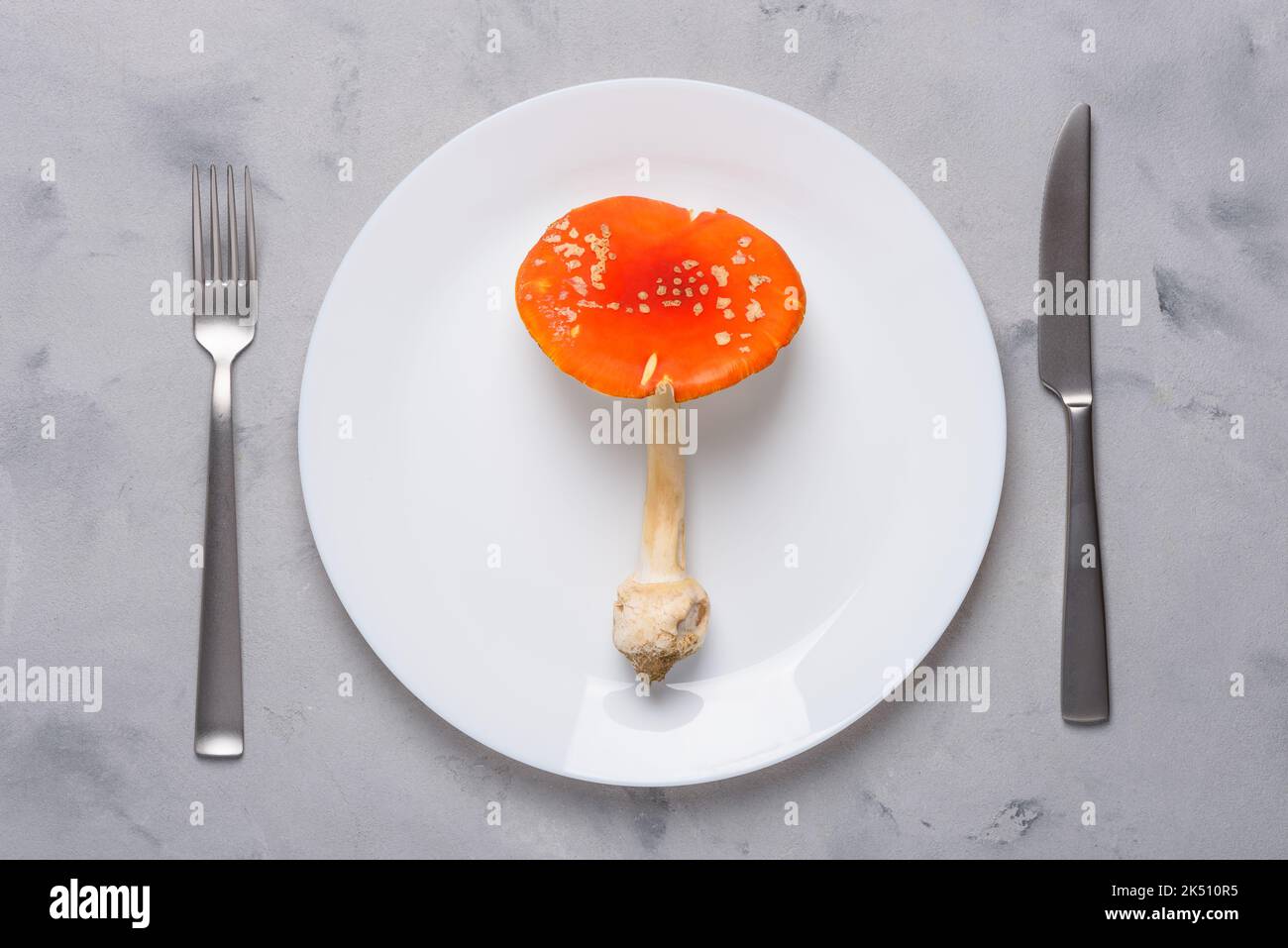 Amanita muscaria mosca agarico fungo velenoso su piatto con forchetta e coltello vista dall'alto. Consumo di funghi allucinogeni concetto Foto Stock