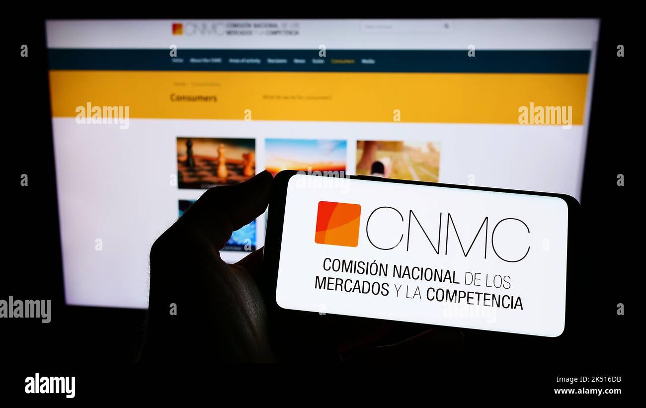 Persona che tiene il cellulare con il logo del regolatore spagnolo concorrenza CNMC sullo schermo di fronte alla pagina web. Messa a fuoco sul display del telefono. Foto Stock