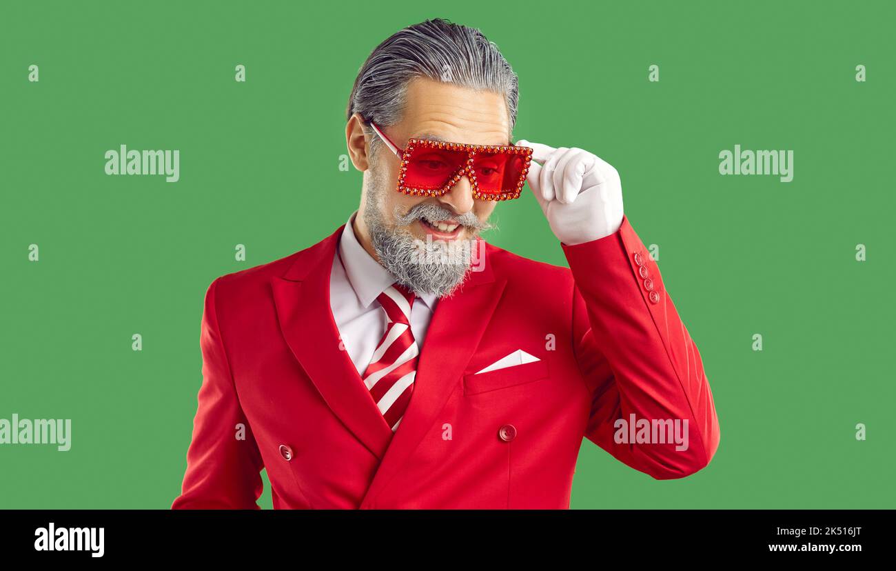 Vecchio uomo in vestito rosso e bicchieri in stile Natale Babbo Natale guardando giù su sfondo verde. Foto Stock