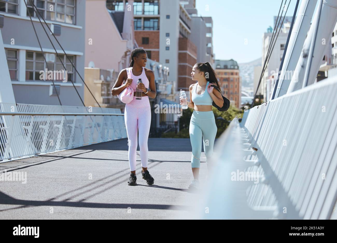 Fitness amici, allenarsi e parlare in una strada della città mentre si cammina verso la palestra con borsa tote per allenarsi, allenarsi e sessioni sportive all'aperto. Diversità Foto Stock