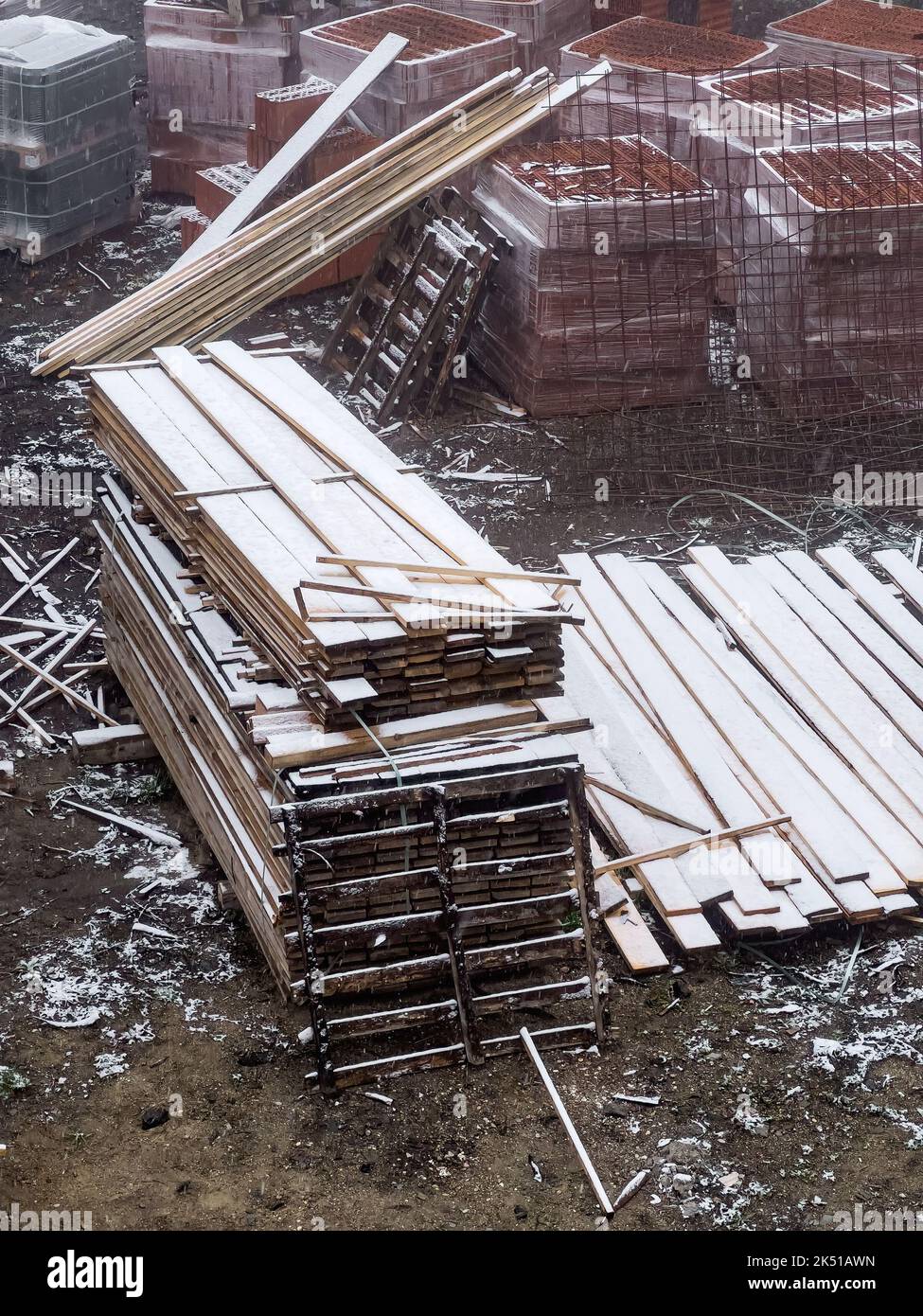 Materiale da costruzione in cantiere durante le nevicate: Tavole, blocchi e tegole, vista ad angolo alto Foto Stock