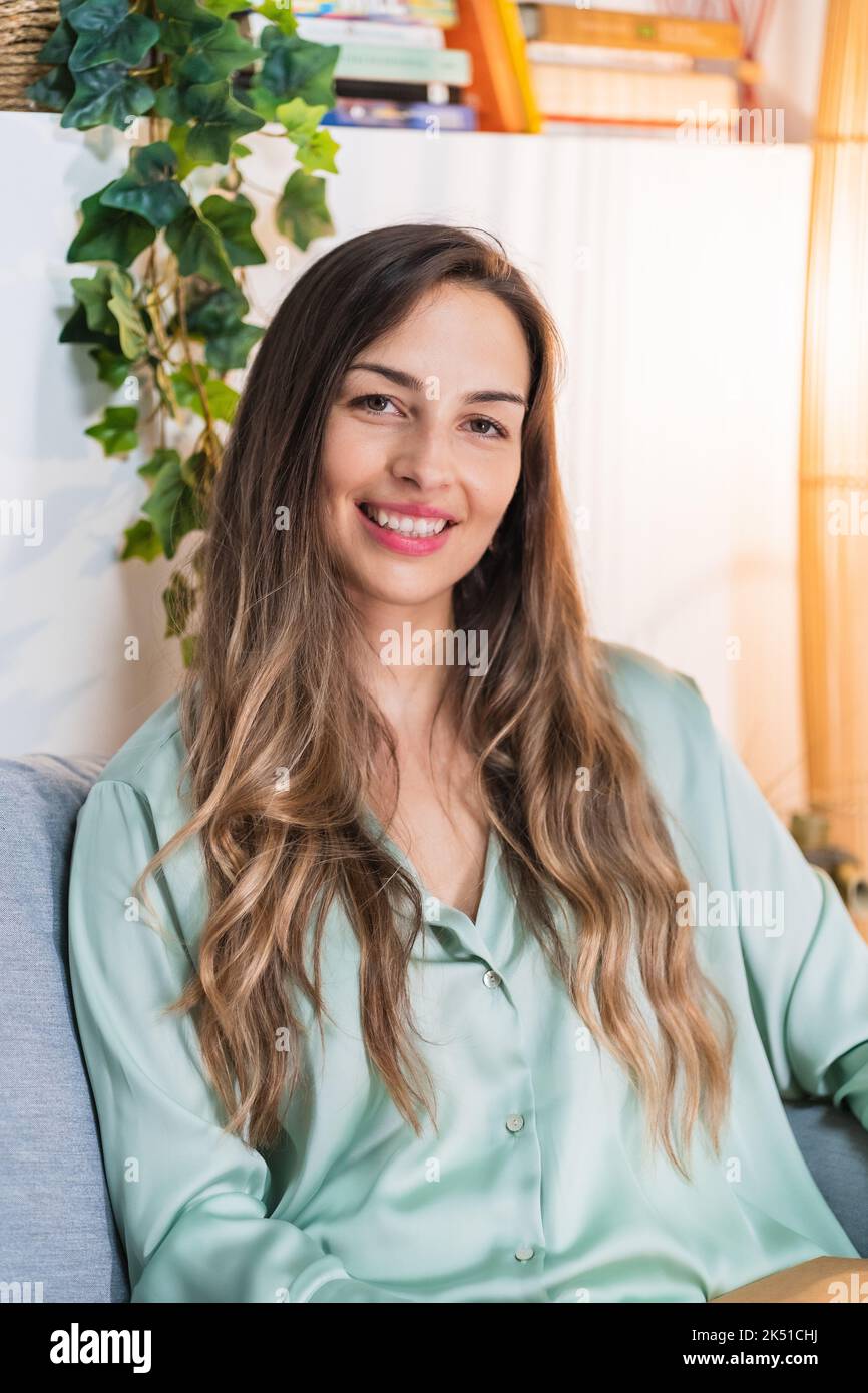 Felice donna freelancer sorridente e guardando la macchina fotografica mentre si siede sul divano a casa Foto Stock